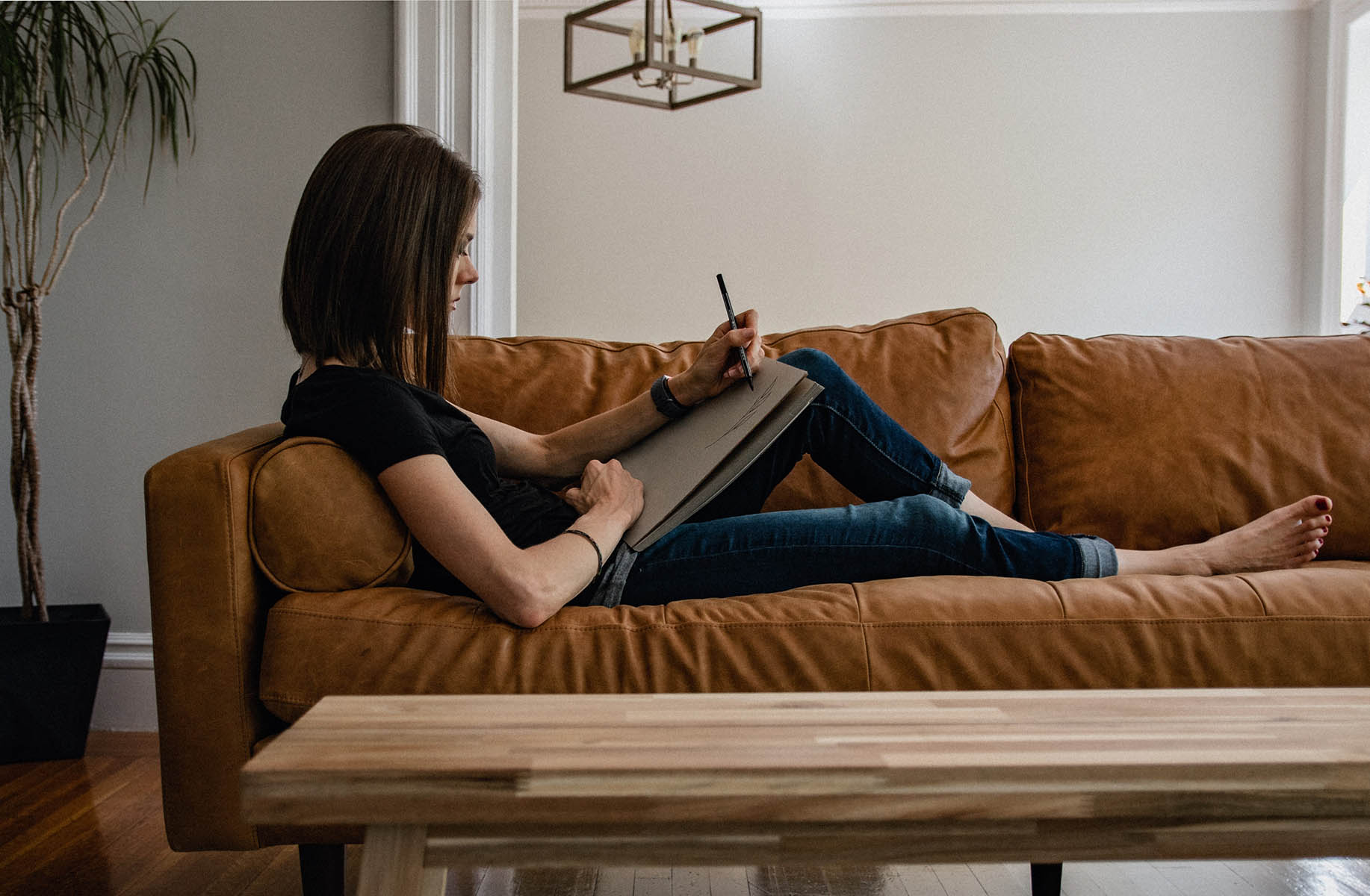 Person in t-shirt and jeans drawing while laying on couch.
