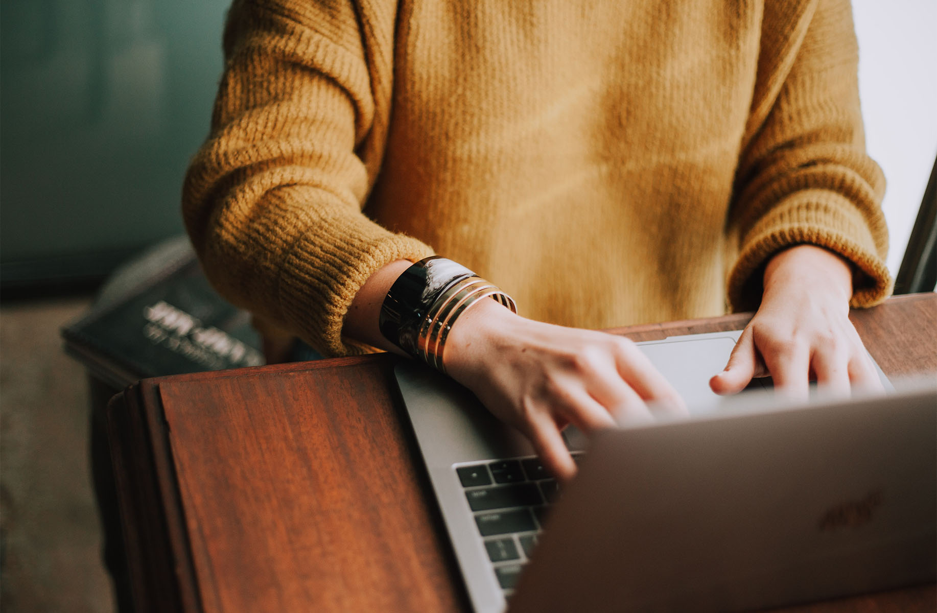 Person in sweater working on laptop at desk.